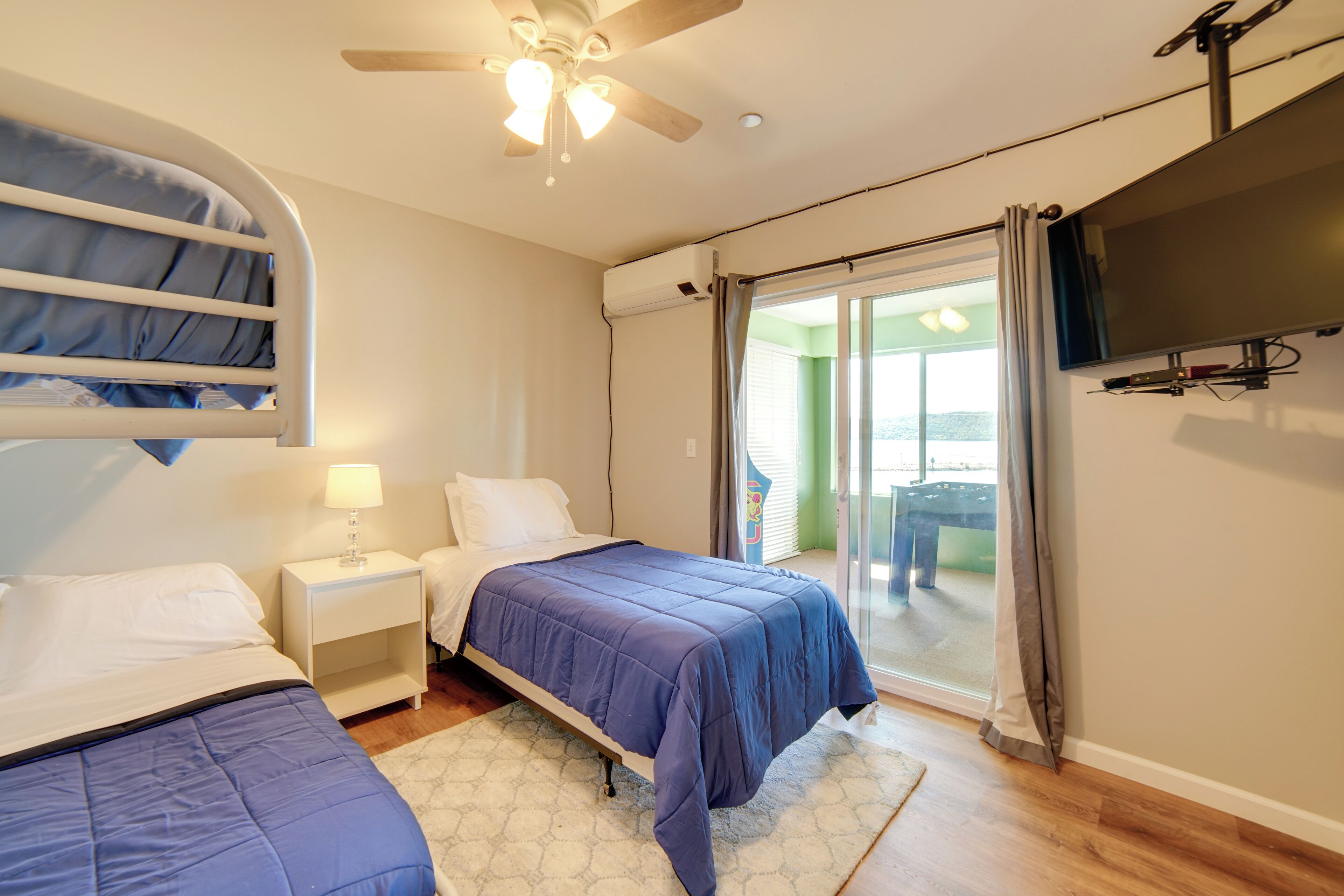A bedroom with two beds, a ceiling fan, a TV, and a sliding glass door to the balcony.