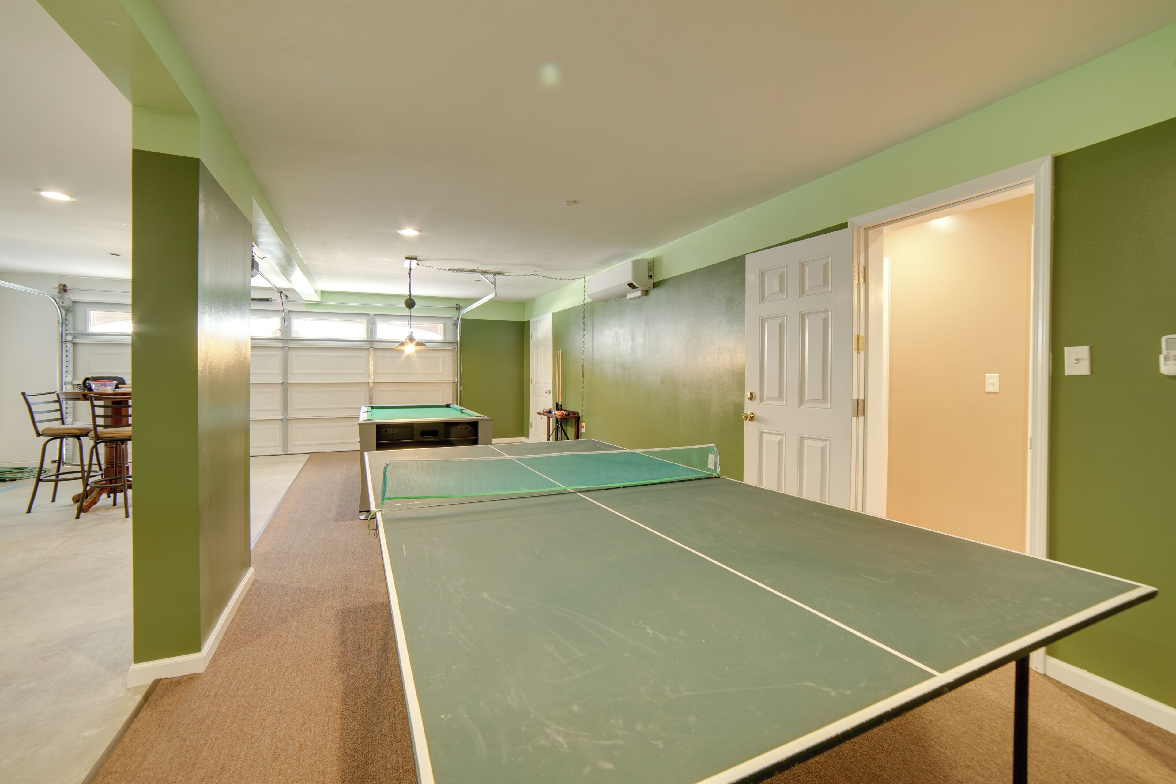 A room with a ping pong table, a pool table, and a door leading to another room.