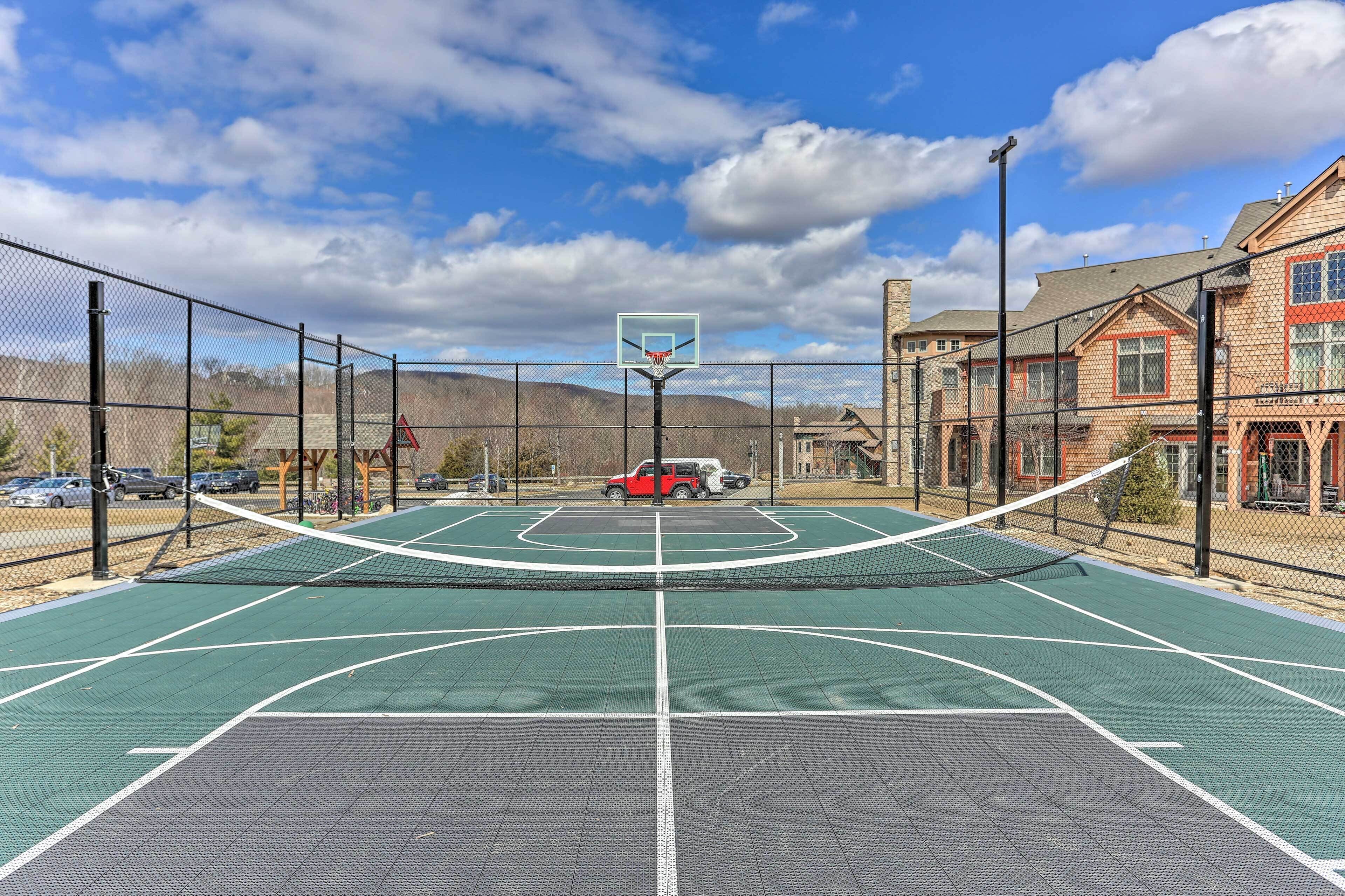 An outdoor basketball court with a net, surrounded by a chain-link fence, and a red vehicle in the background.