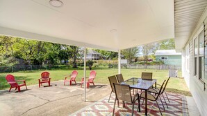 Eine überdachte Terrasse mit Tisch und Stühlen, einem gemusterten Teppich und Blick auf eine grüne Wiese und Bäume.
