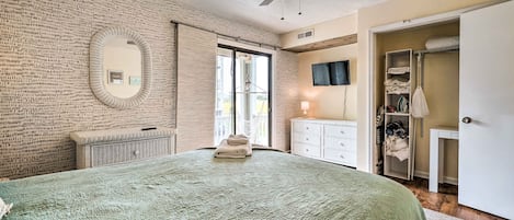 A bedroom with a large bed, a ceiling fan, a mirror, a wardrobe, and a television on the wall.