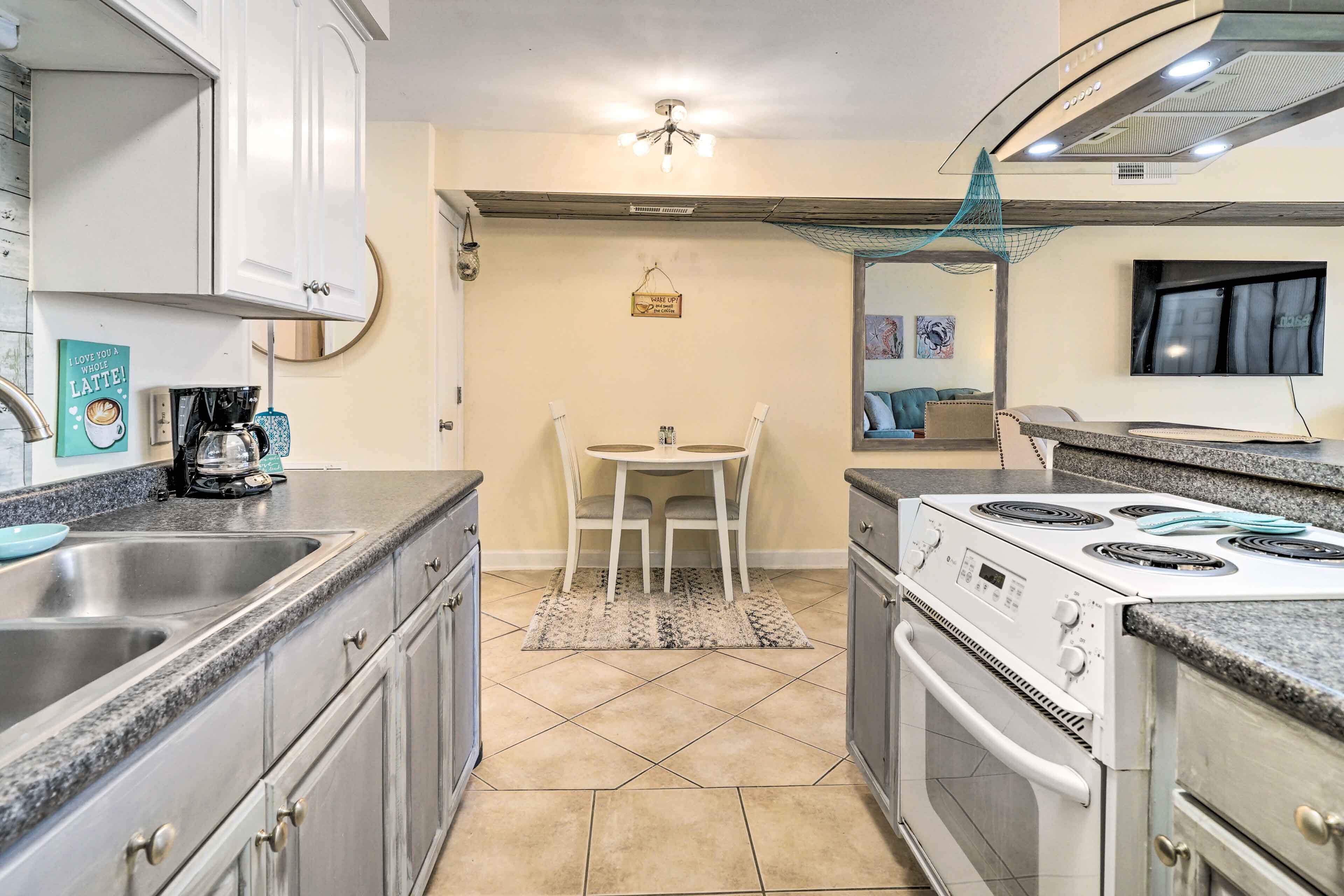 A compact kitchen with a stove, sink, and white cabinets. A small table with chairs is in the center.