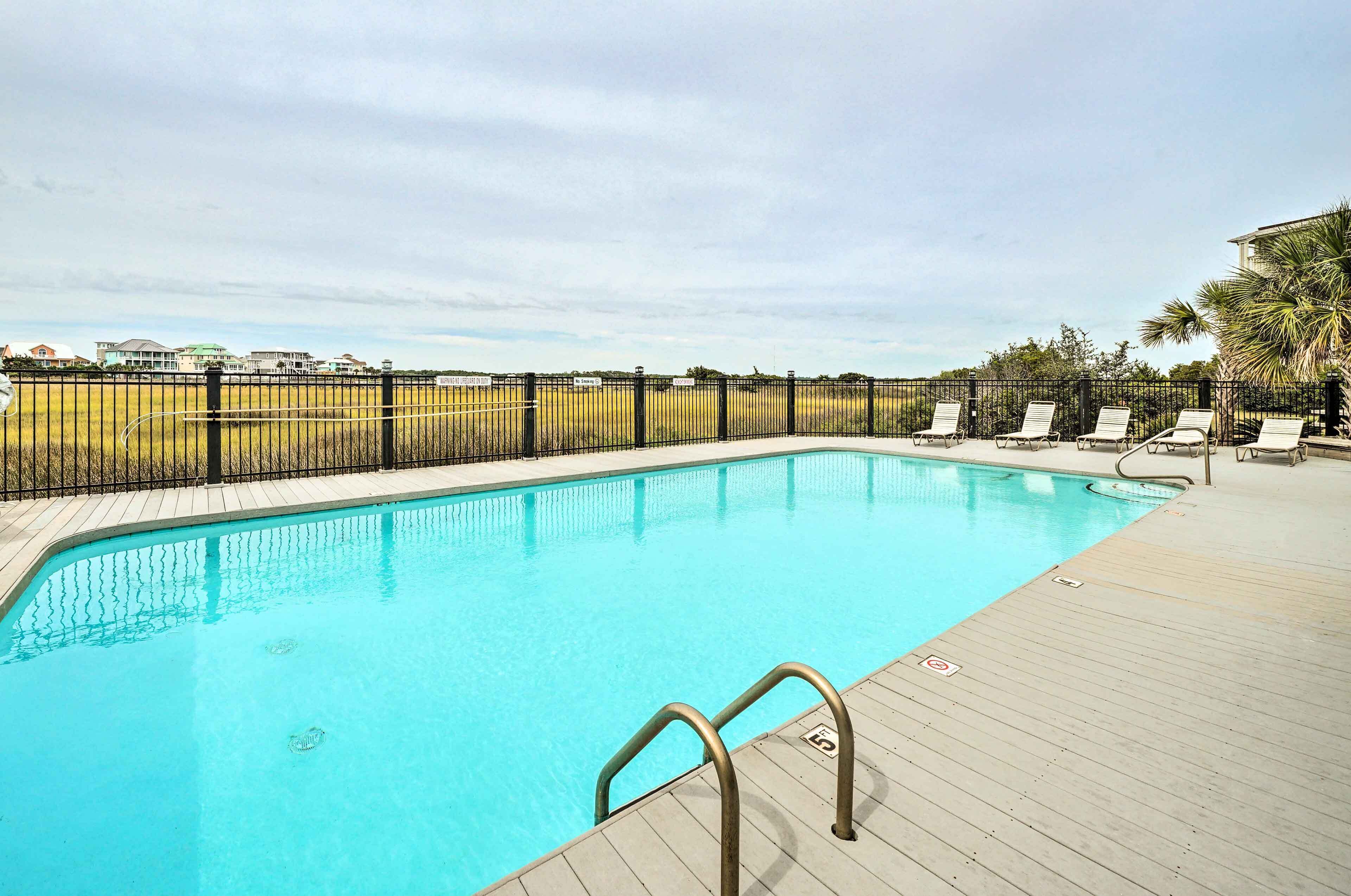 A swimming pool with a wooden deck and lounge chairs, surrounded by a fence and palm trees.