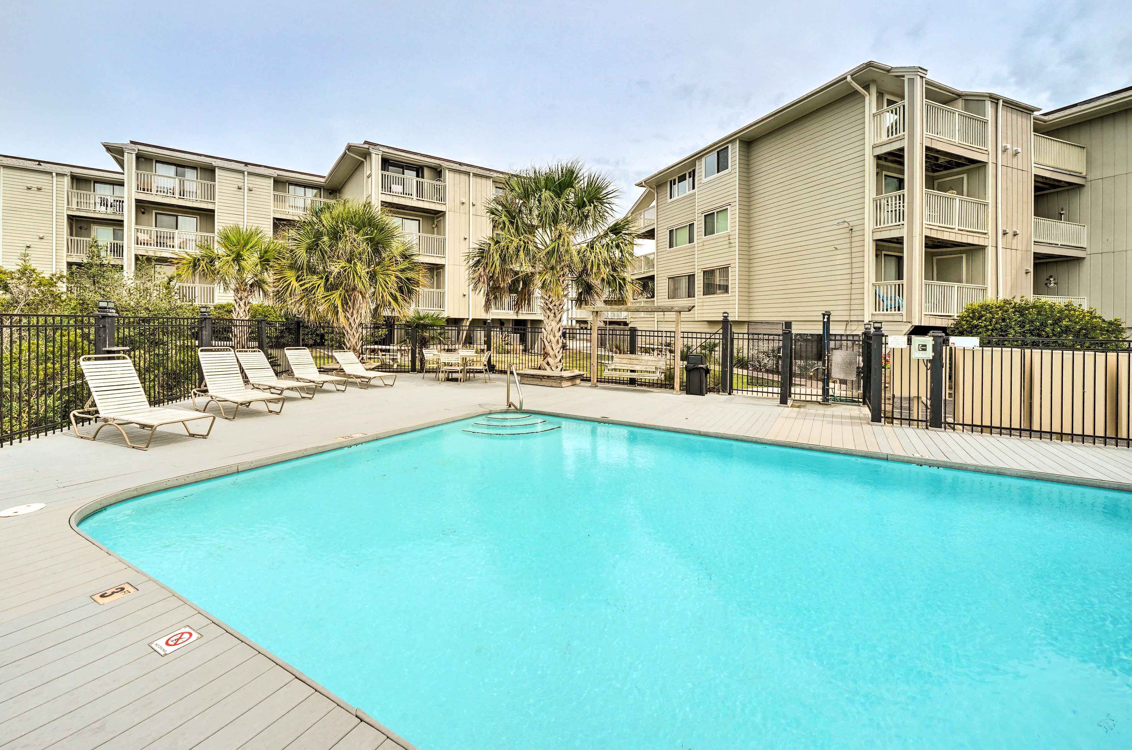 A swimming pool with lounge chairs and a palm tree, surrounded by apartment buildings.