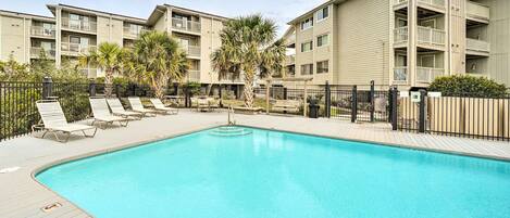 A swimming pool with lounge chairs and a palm tree, surrounded by apartment buildings.