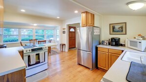 A modern kitchen with a built-in oven, a refrigerator, wooden cabinets, and a dining area with a table and chairs. - Charming Indianola Home: Walk to Town! (Indianola)