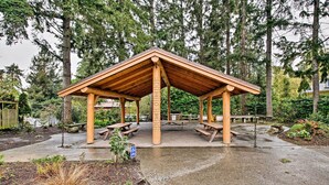 A wooden pavilion with benches and picnic tables, surrounded by trees and a garden area. - Charming Indianola Home: Walk to Town! (Indianola)