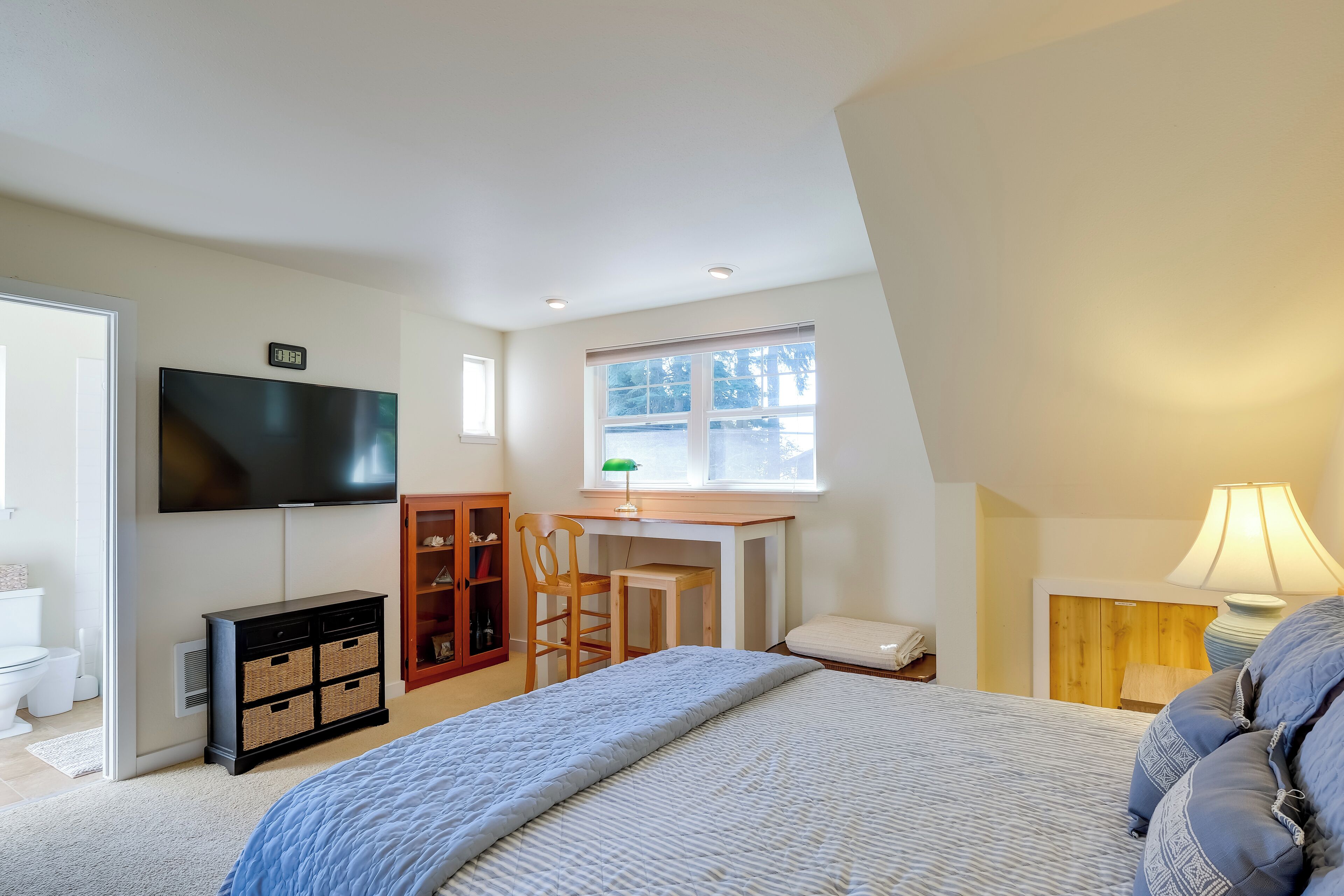 Un dormitorio con cama, escritorio, televisión, ventana y lámpara.