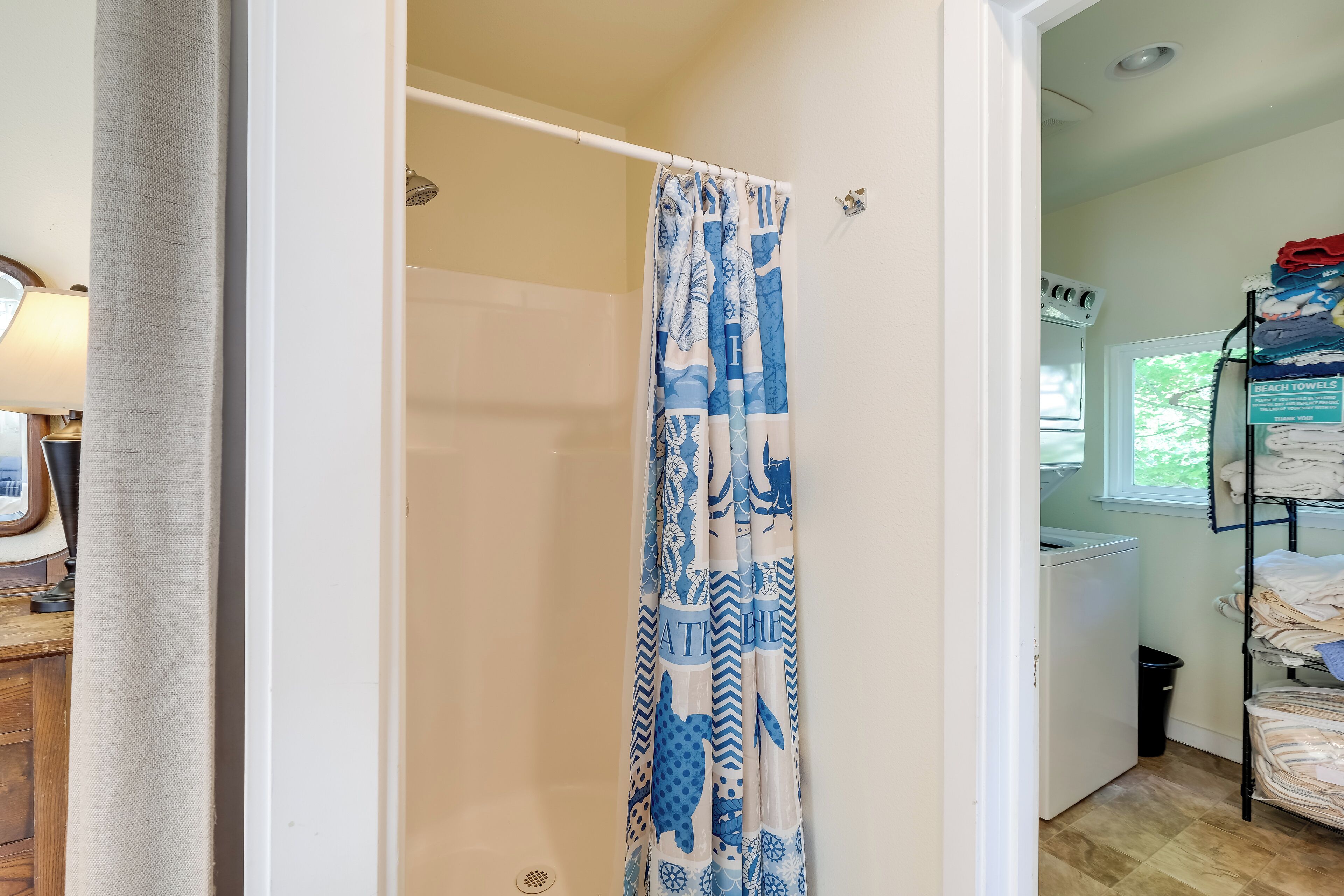 A bathroom with a shower curtain, a washing machine, and a shelf with folded towels.
