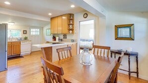 A spacious kitchen with wooden cabinets, a dining table, and a view of the outdoors. - Charming Indianola Home: Walk to Town! (Indianola)