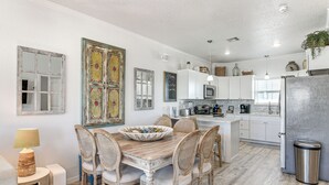Uma cozinha moderna com armários brancos, uma geladeira de aço inoxidável e uma área de refeições com mesa de madeira e cadeiras de vime.