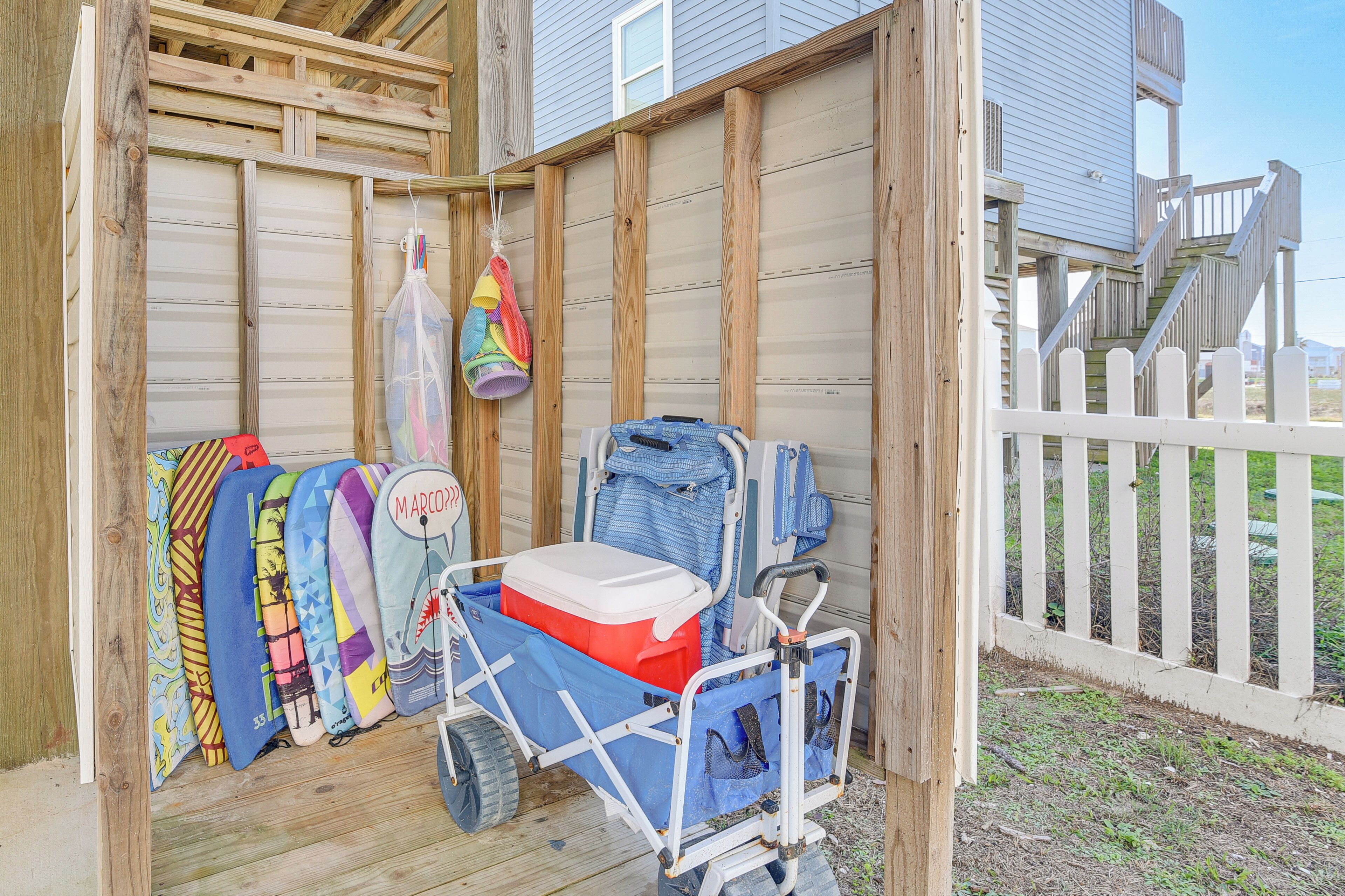A wooden structure with a white fence, a cart with a cooler, and colorful surfboards.