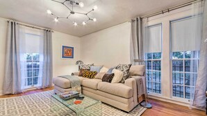 A living room with a beige sofa, patterned rug, glass coffee table, and a ceiling light fixture.