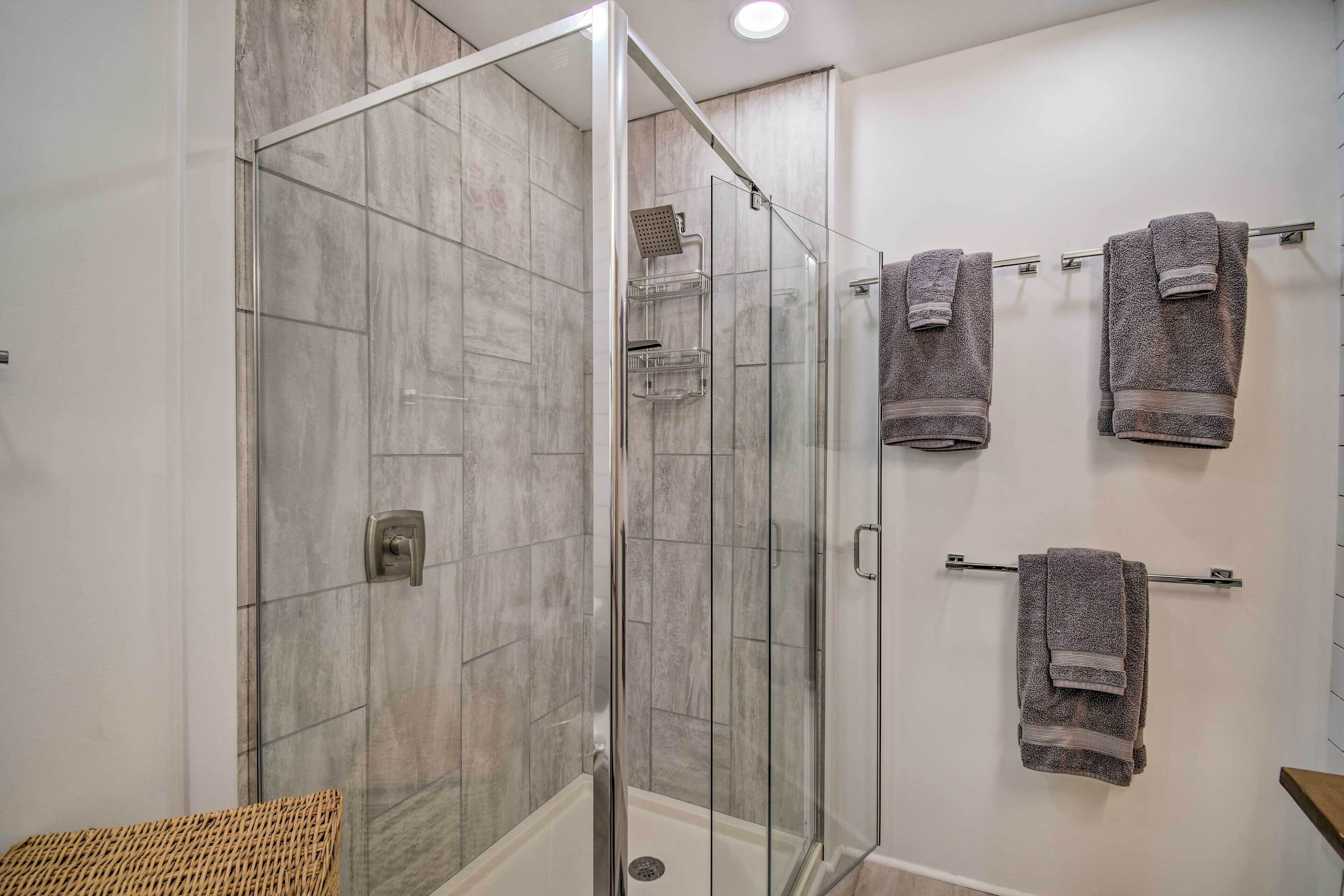 Une salle de bain moderne avec une douche à parois de verre, un porte-serviettes avec plusieurs serviettes et un panier en osier.