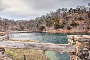 A rustic cabin on a hill overlooking a calm lake, surrounded by trees and stone structures.