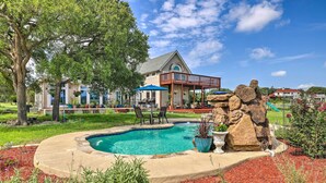 Une piscine entourée d’une terrasse en pierre, avec une terrasse en bois et des chaises à proximité.