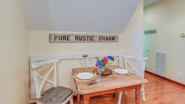 A dining area with rustic decor, including a wooden table and chairs, a sign reading "PURE RUSTIC CHARM", and a small vase with flowers. - 5 Mi to Dtwn: Serene Couple's Retreat in Franklin! (Franklin)