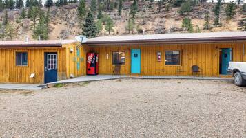 A wooden building with multiple doors and windows, a gravel driveway, and a mountainous backdrop.
