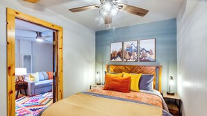 A bedroom with a bed, a ceiling fan, a wooden headboard, and a colorful rug. - Steps to Main Street! Cozy Red River Getaway (Red River)