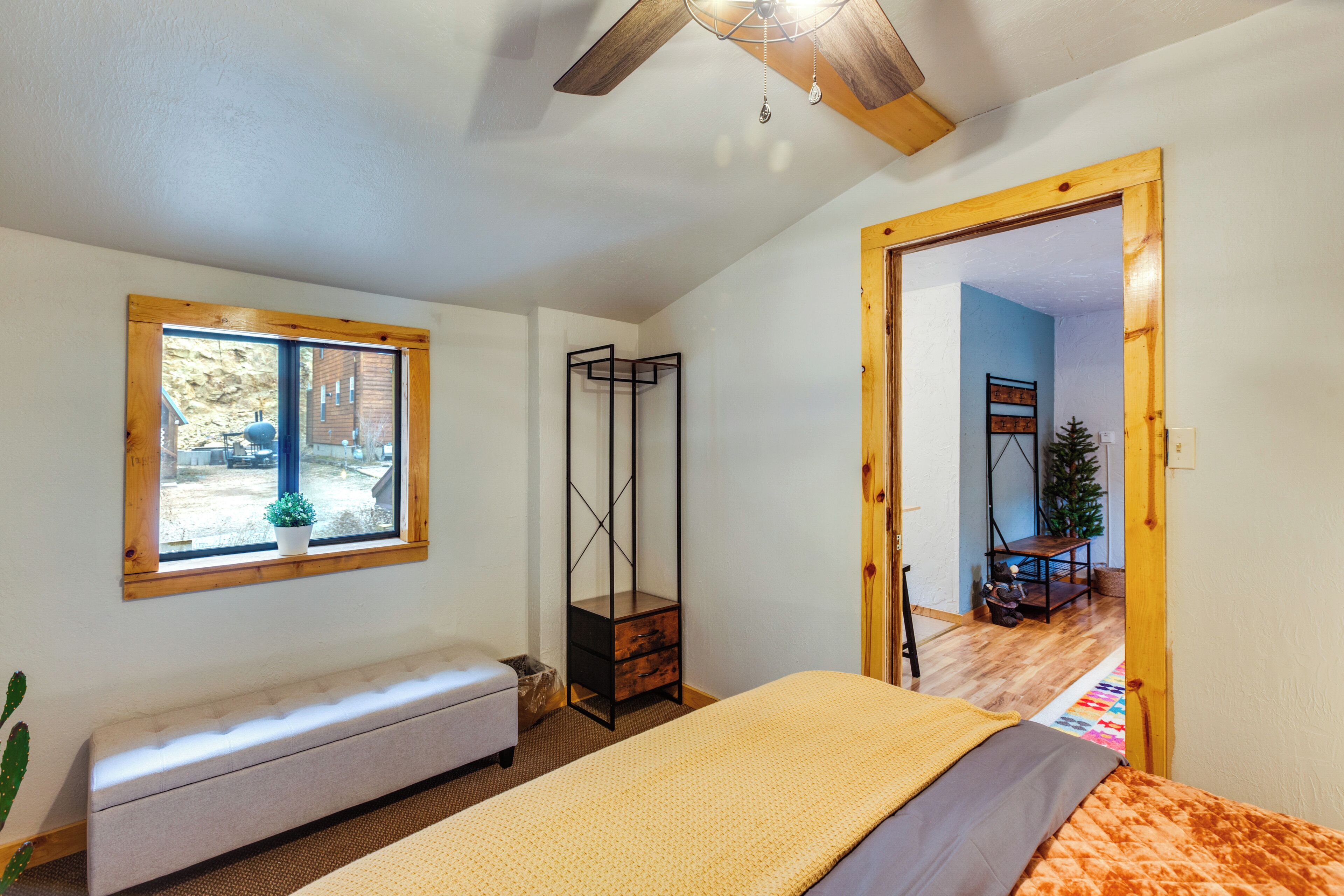 Un dormitorio con una cama, un banco, una ventana y una puerta de madera que da a otra habitación.
