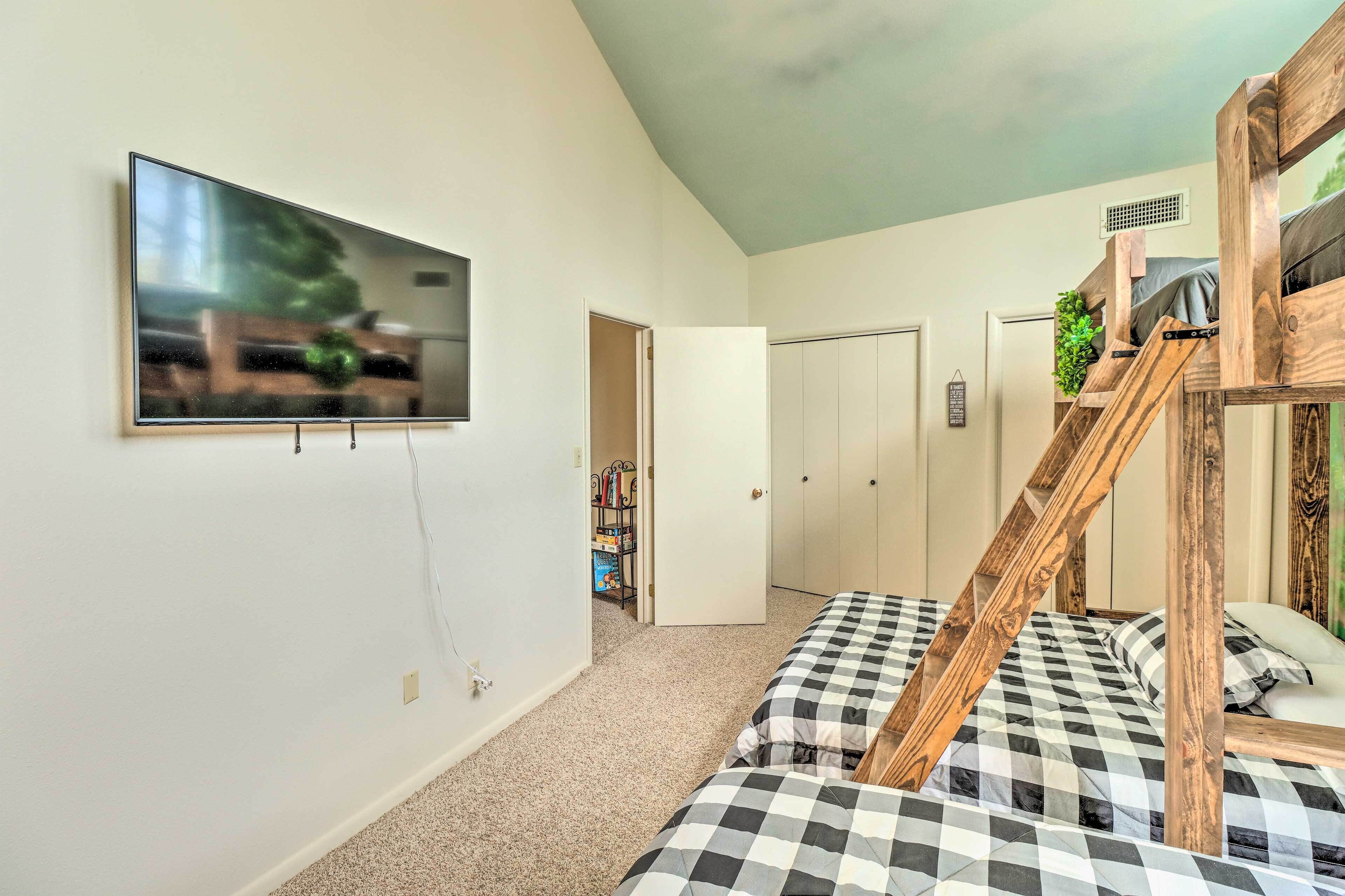 Ein Schlafzimmer mit Etagenbett, einem an der Wand montierten Fernseher und einer Tür zu einem weiteren Raum.