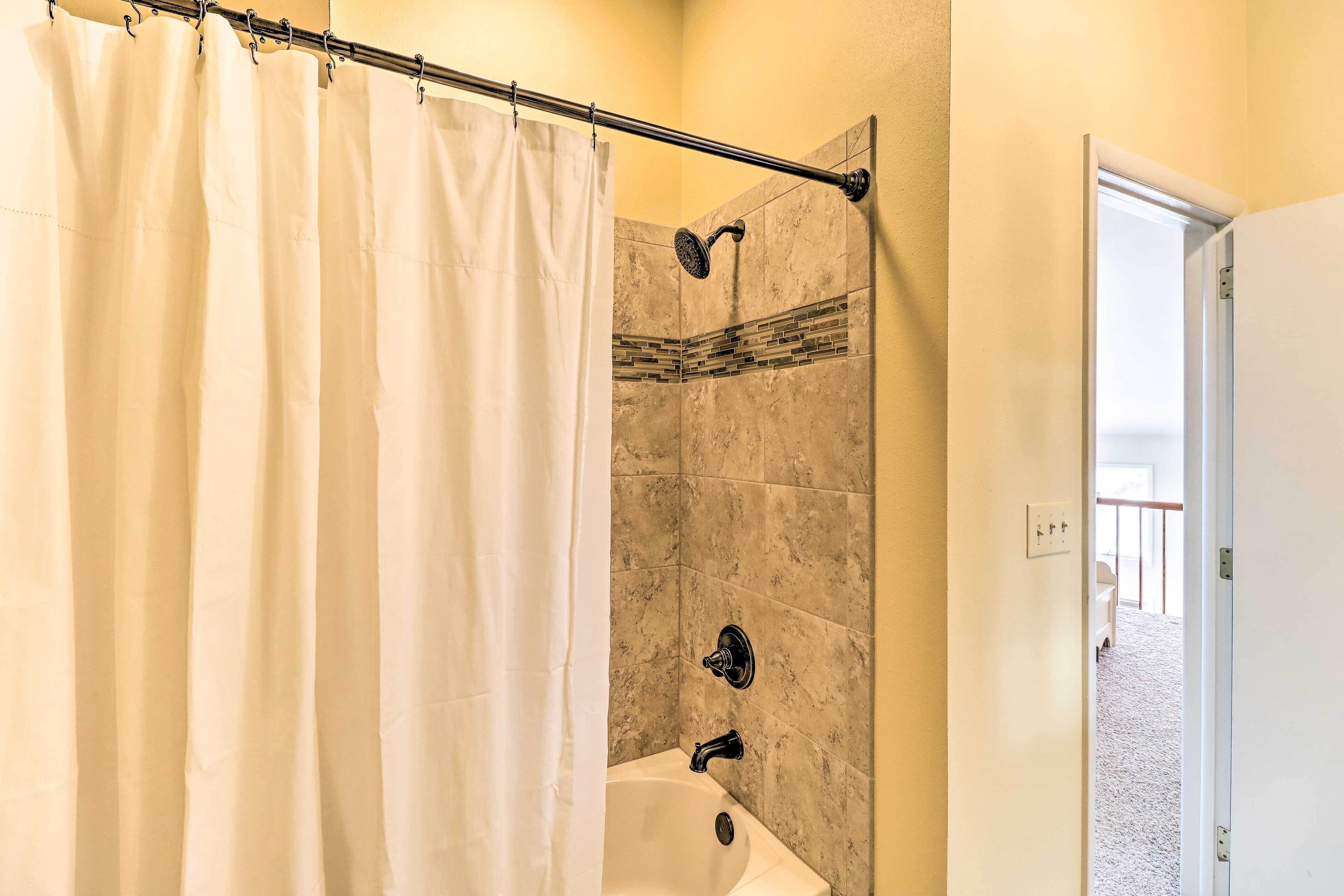A bathroom with a shower, a bathtub, and a door leading to another room.