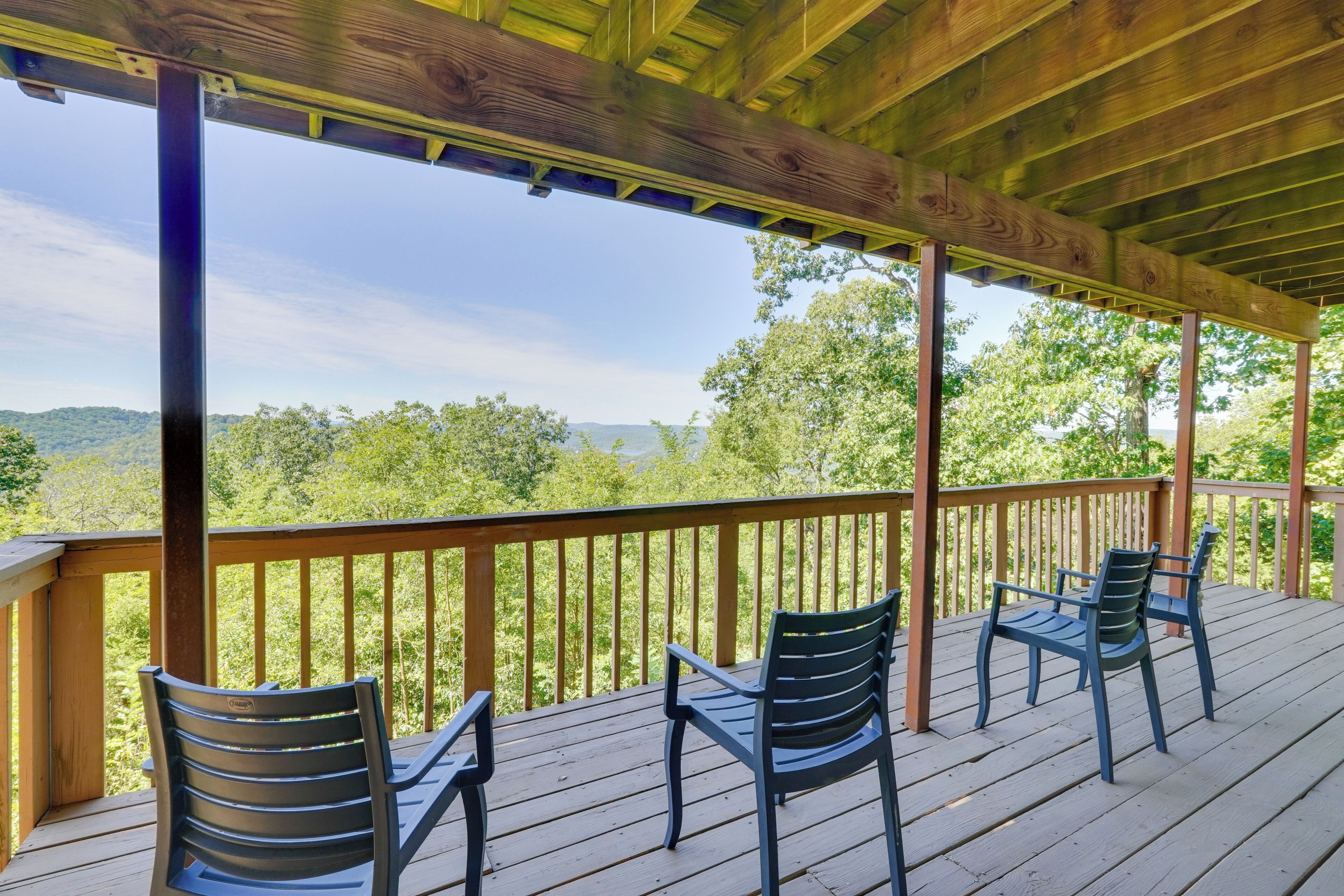 Eine Holzterrasse mit Geländer, zwei Stühlen und Blick auf eine bewaldete Landschaft.