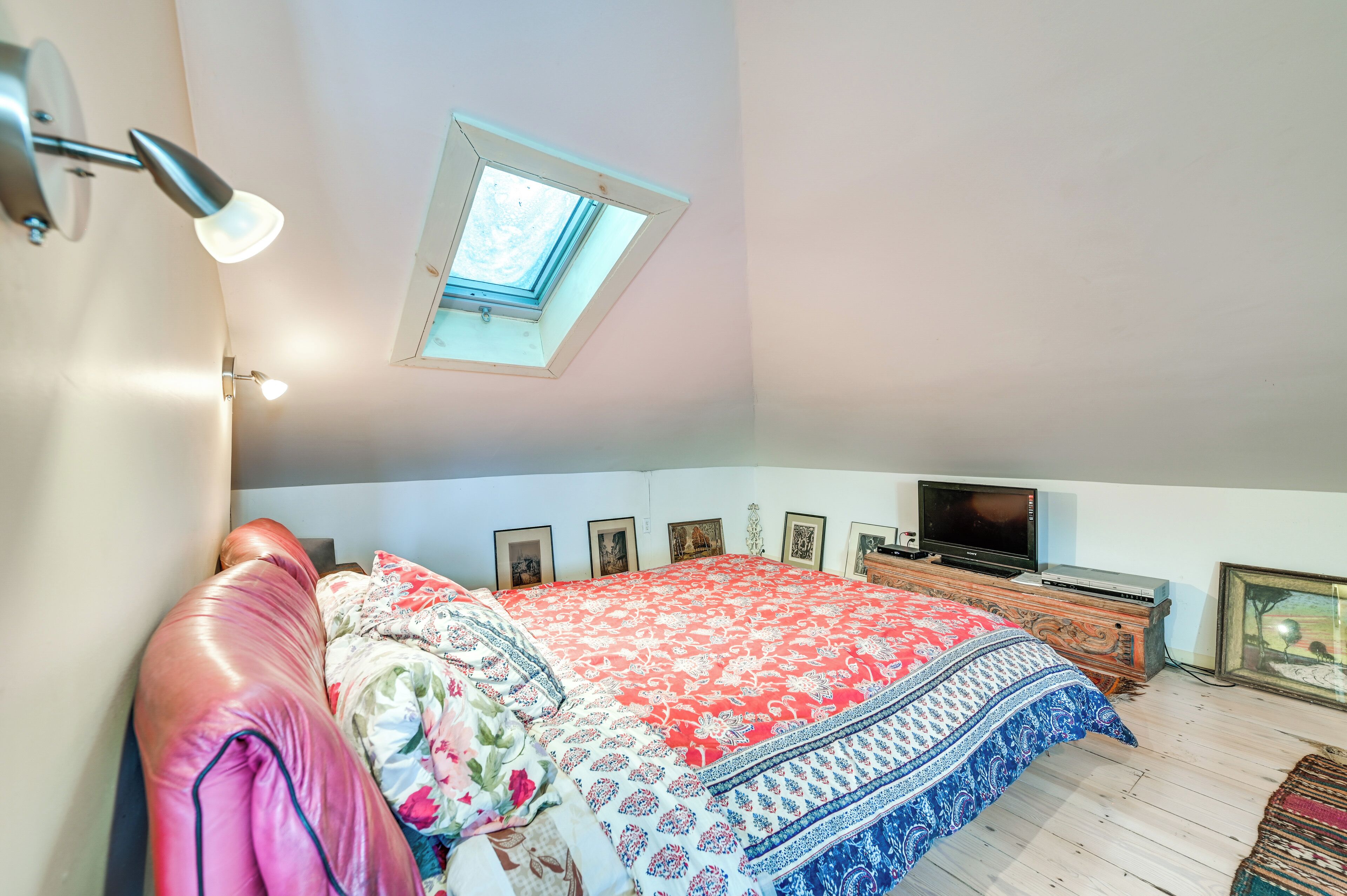 Une chambre avec un puits de lumière, un lit avec une literie à motifs floraux, une télévision et une commode.