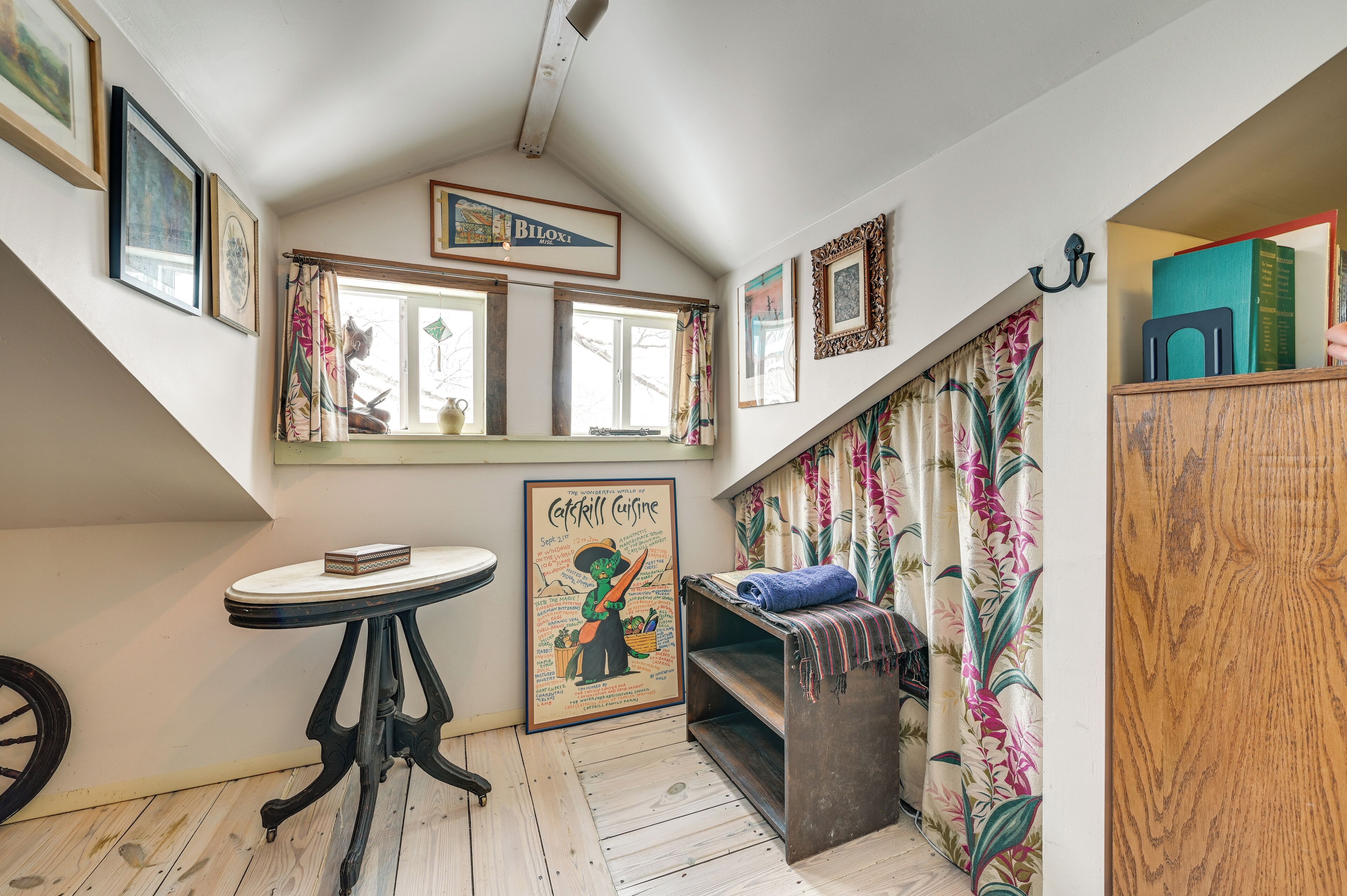 A cozy room with a sloped ceiling, a small table with a book, a bench with a blanket, and a window with curtains.