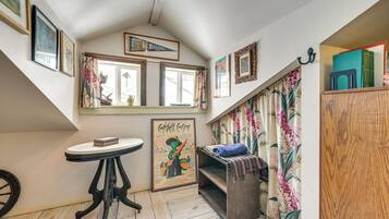 A cozy room with a sloped ceiling, a small table with a book, a bench with a blanket, and a window with curtains.