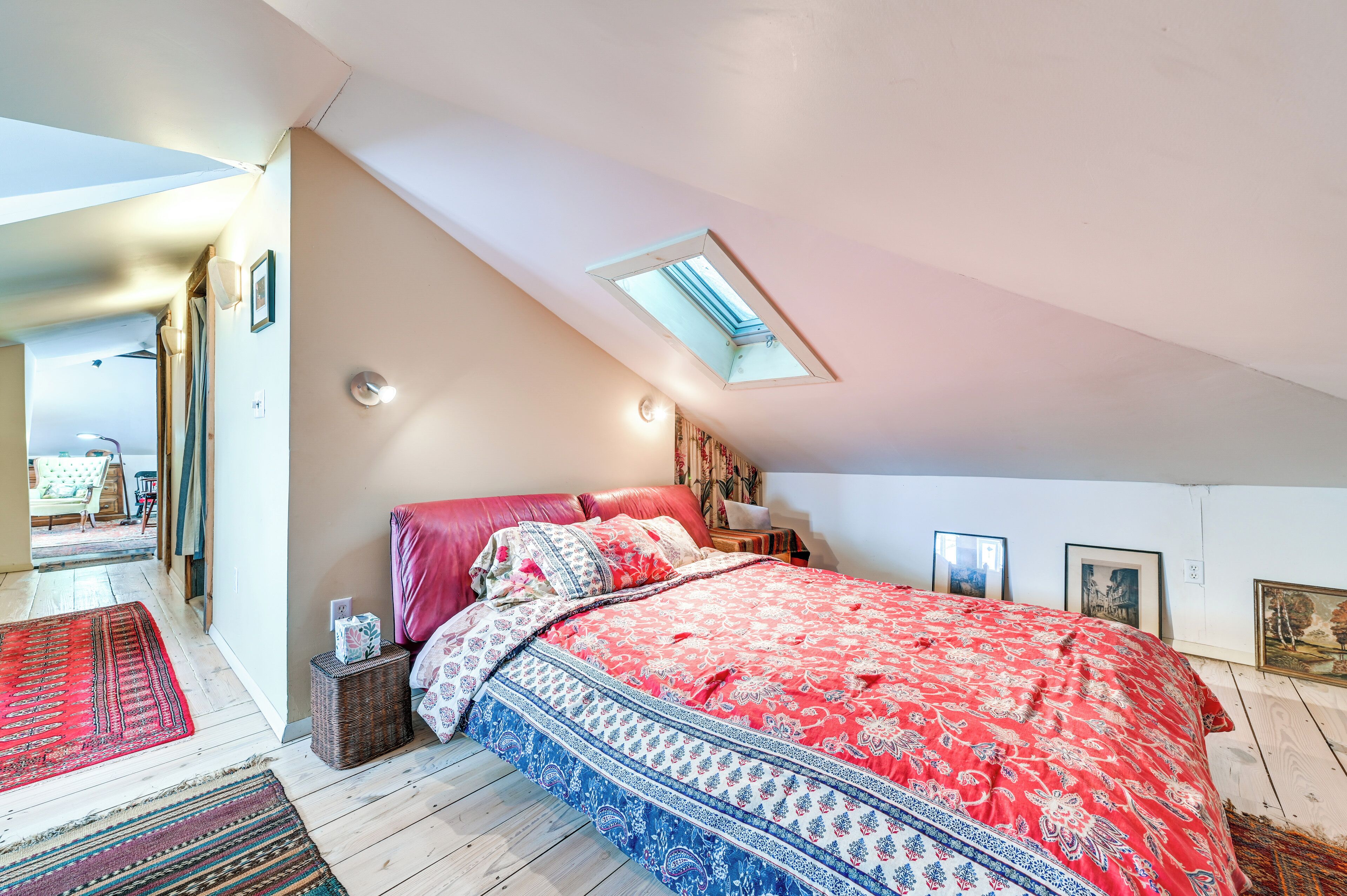 A bedroom with a skylight, a large bed with patterned bedding, a bedside table, and a rug.