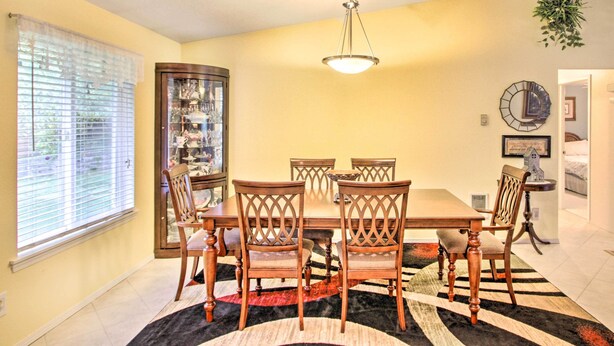 A dining room with a wooden table and chairs, a chandelier, and a large window with blinds.