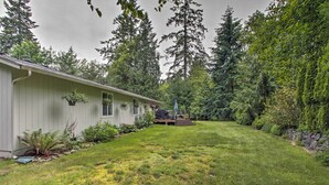 A house with a well-maintained lawn, a deck, and a variety of plants and trees around it.