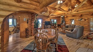 Ein rustikales Holzhaus-Interieur mit einem Holzespeisesaal, Stühlen, einer Couch und einem Fernseher.