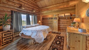 Ein Schlafzimmer in einer Blockhütte mit einem Bett, einem Schminktisch, einer Lampe und einem Fenster.