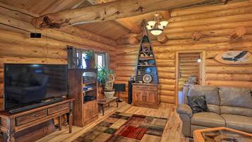 A log cabin interior with a television, wooden furniture, a fireplace, and a cozy seating area.