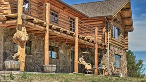 Eine Blockhütte mit Steinverkleidung, einer Veranda mit Schaukelstuhl und einem großen Baumstumpf.
