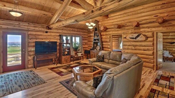 Ein rustikaler Innenraum einer Blockhütte mit einem großen Fernseher, einem Ledersofa, Holzdielen und einem Kamin.