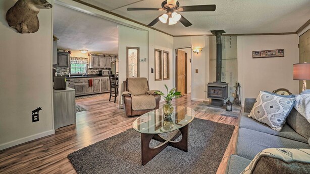 A spacious living room with a glass coffee table, a ceiling fan, a fireplace, and a kitchen in the background. - Cozy Hale Home Between Long & Loon Lakes! (Hale)