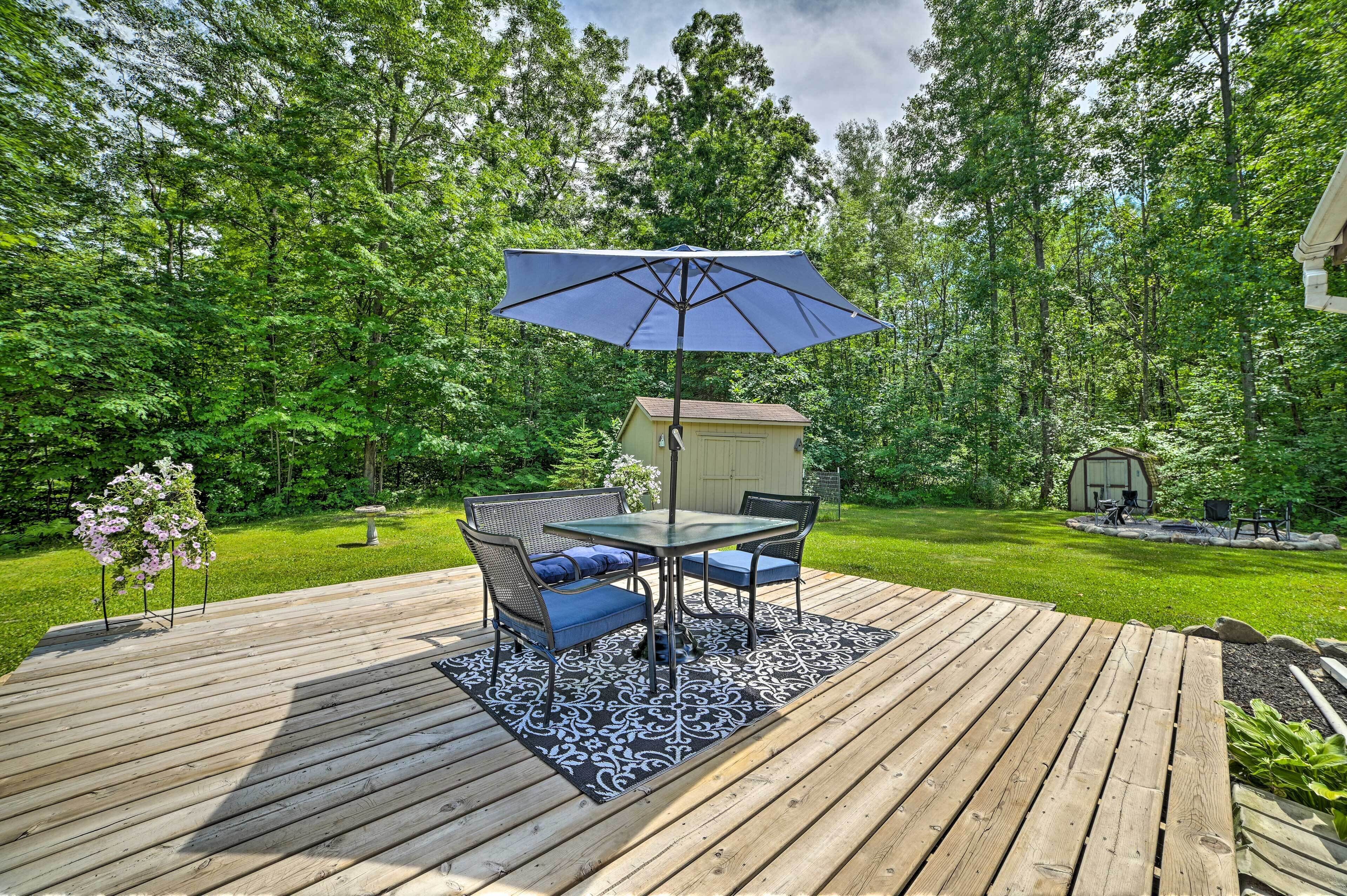 A wooden deck with a table and chairs, an umbrella, and a shed in a lush green backyard.