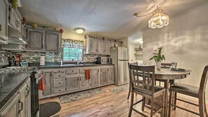 A kitchen with wooden cabinets, a granite countertop, and a dining area with a table and chairs. - Cozy Hale Home Between Long & Loon Lakes! (Hale)