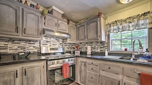 Une cuisine avec des meubles de couleur bois clair, une cuisinière en acier inoxydable et une fenêtre donnant sur un paysage verdoyant.