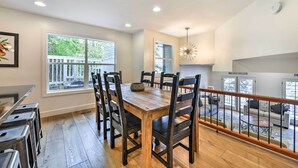 A dining area with a wooden table and chairs, large windows, and a view of a deck.