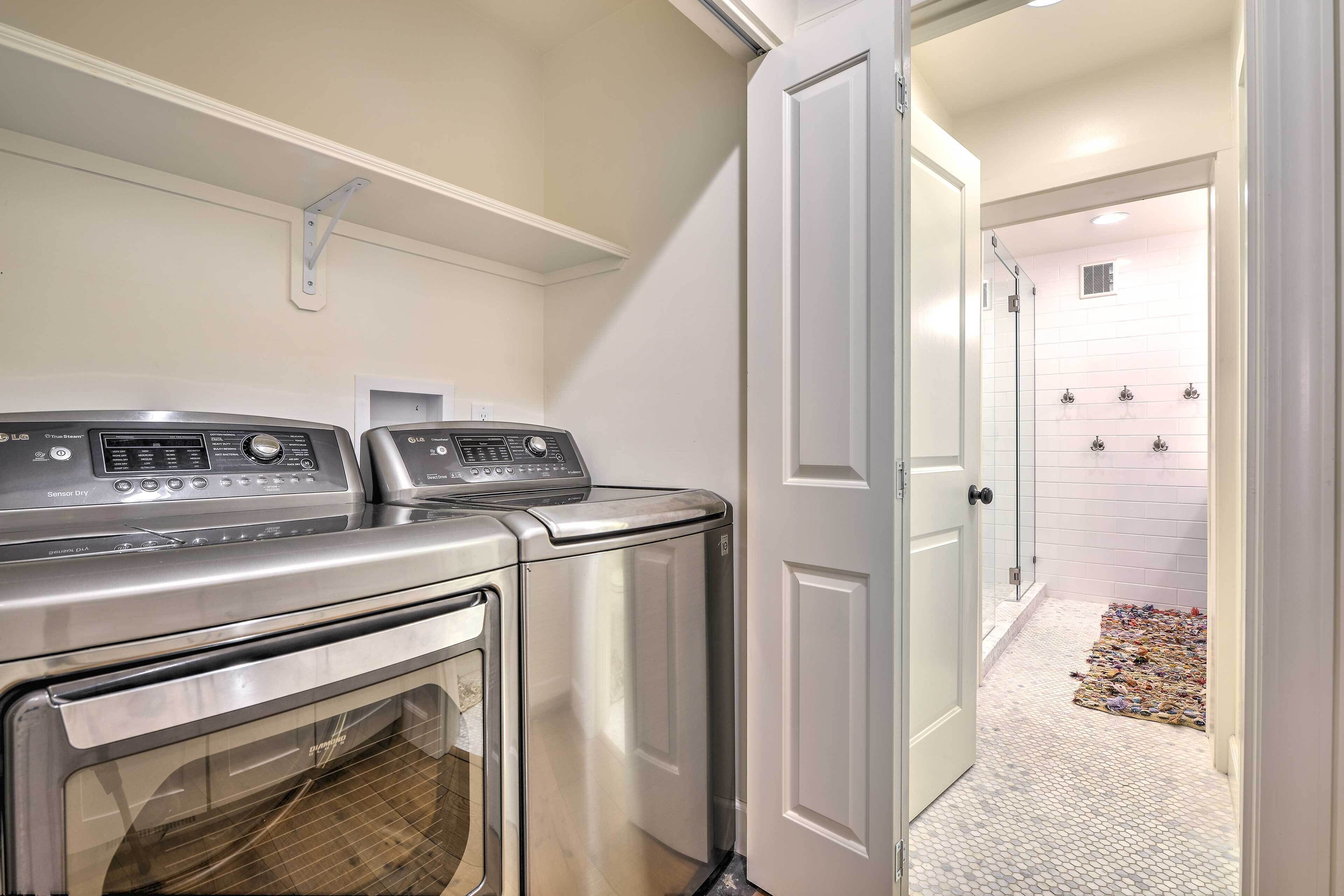 A laundry area with two front-loading washing machines and a dryer, a white door leading to a tiled bathroom, and a small rug on the bathroom floor.