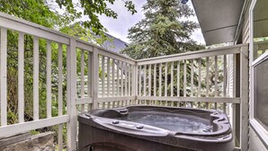 A hot tub on a wooden deck with a white railing, surrounded by greenery.