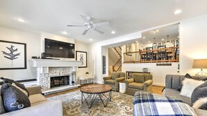 A spacious living room with a fireplace, a ceiling fan, and a staircase leading to an upper level.