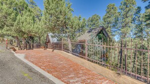 A paved walkway with a brick pattern leading to a fenced area with a small building. - Cozy Ruidoso Cottage w/ Deck - 10 Min to Village! (Ruidoso)