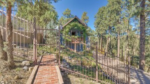 A rustic cabin with a brick pathway leading to a gated entrance, surrounded by tall pine trees. - Cozy Ruidoso Cottage w/ Deck - 10 Min to Village! (Ruidoso)