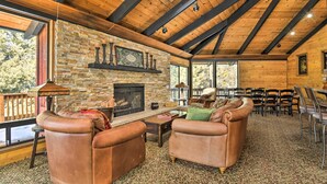 Ein gemütliches Blockhaus-Interieur mit Kamin aus Stein, Ledersofas und einem Essbereich mit Gartenmöbeln.