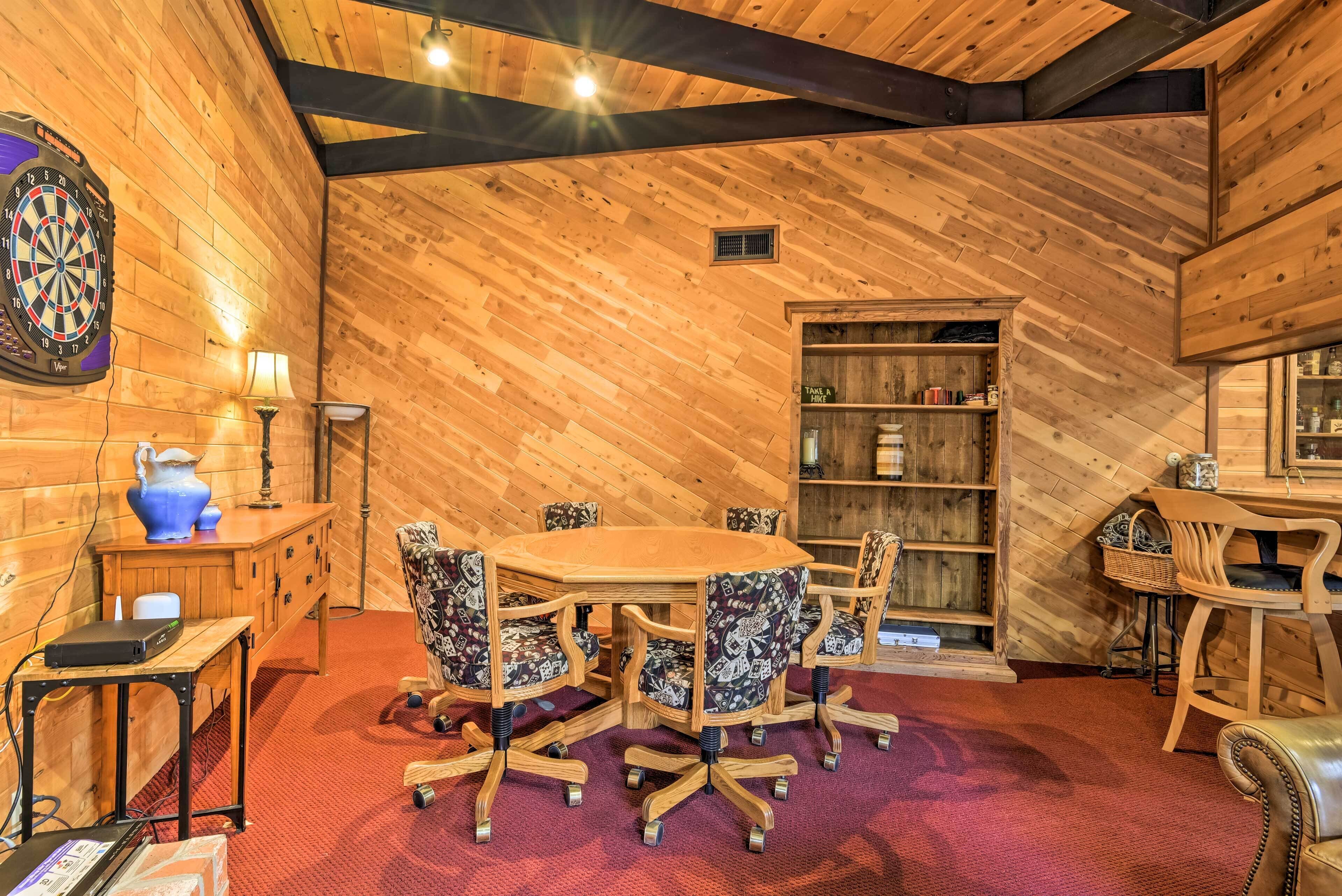 A wooden interior with a round table and chairs, a dartboard, and a bookshelf.